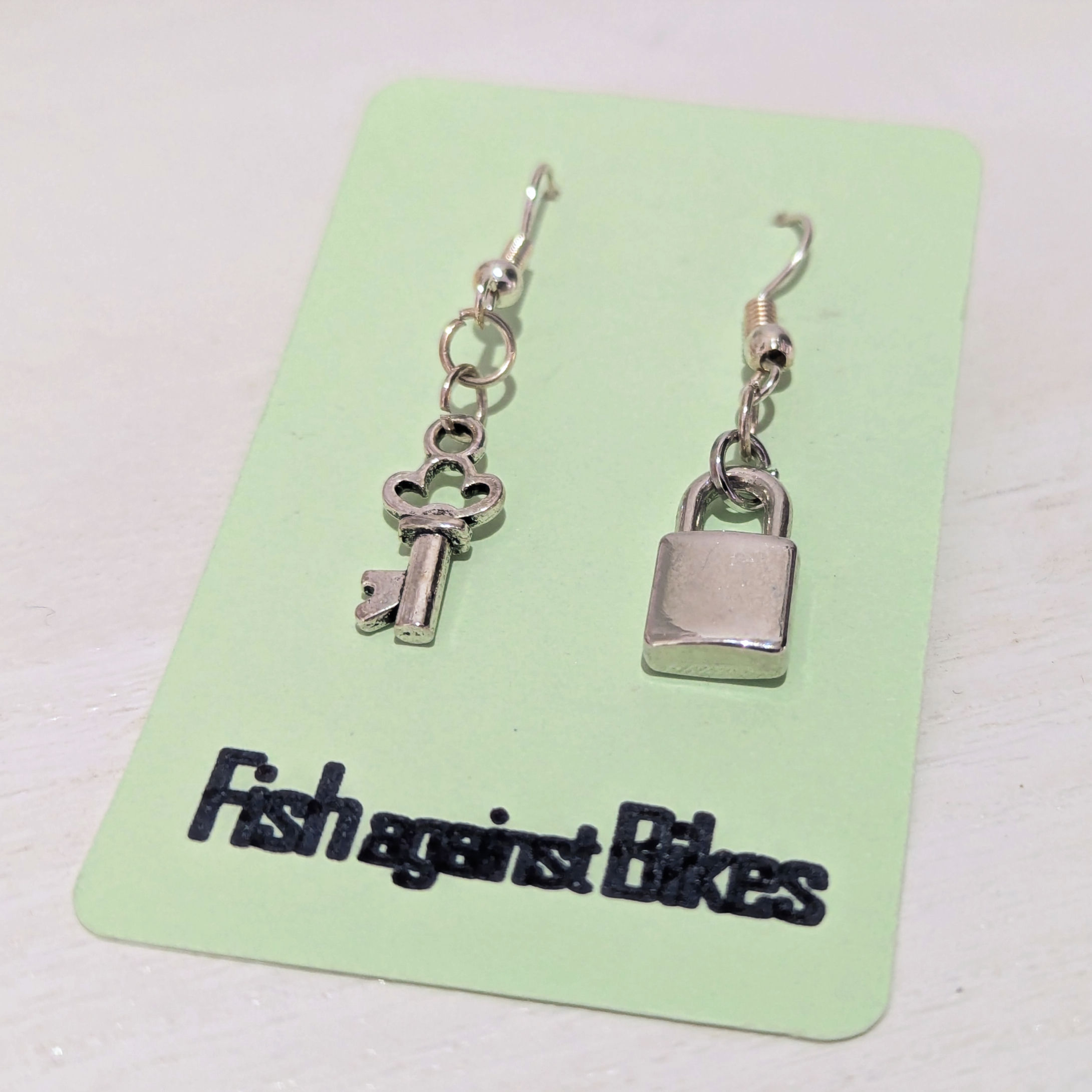 Silver key charm earring and silver lock charm earring as a non-matching pair on backing card.