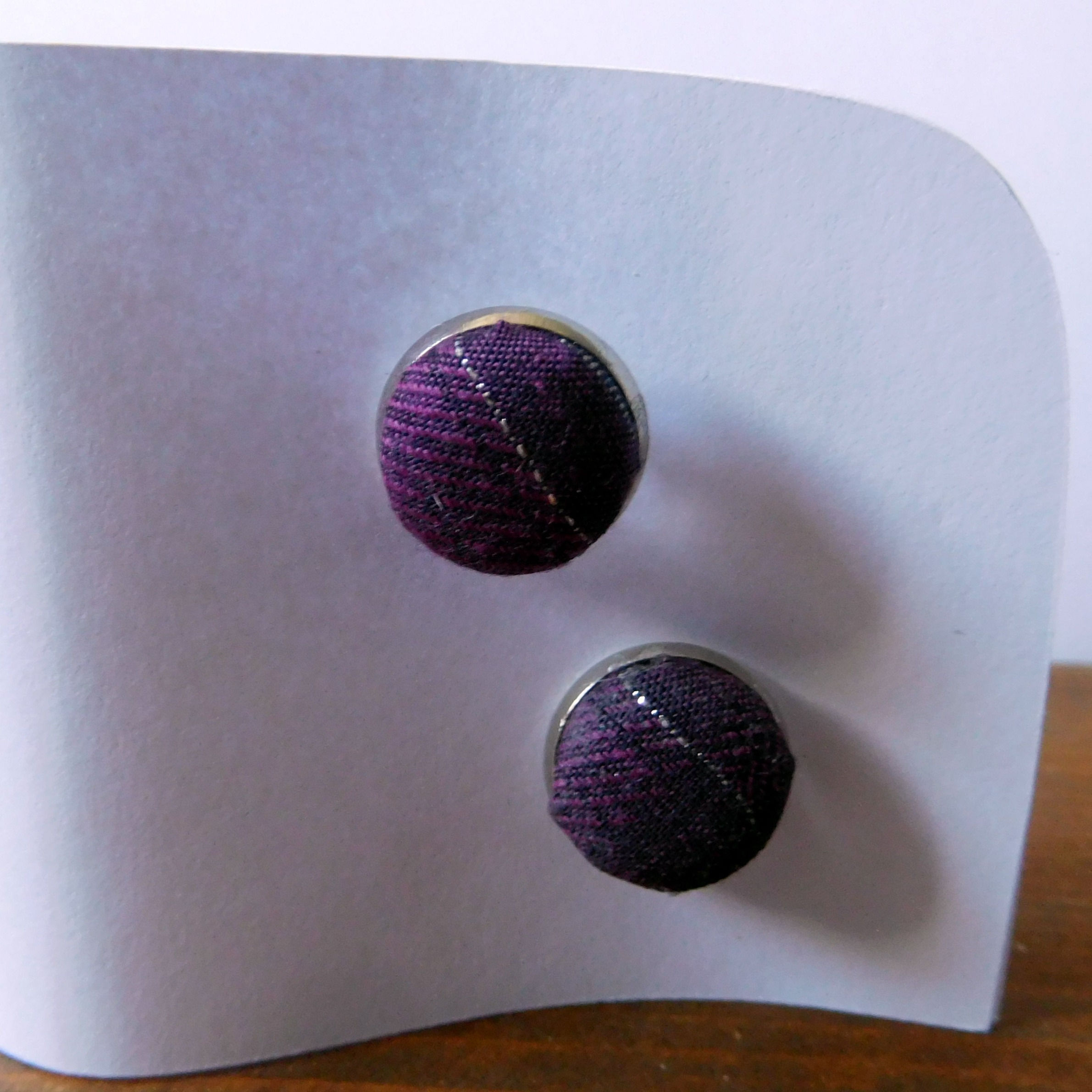 Purple fabric cufflinks with silver stripe on white backing card.