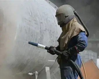 Worker performing abrasive blasting on large tank, industrial setting, abrasive blasting wa.