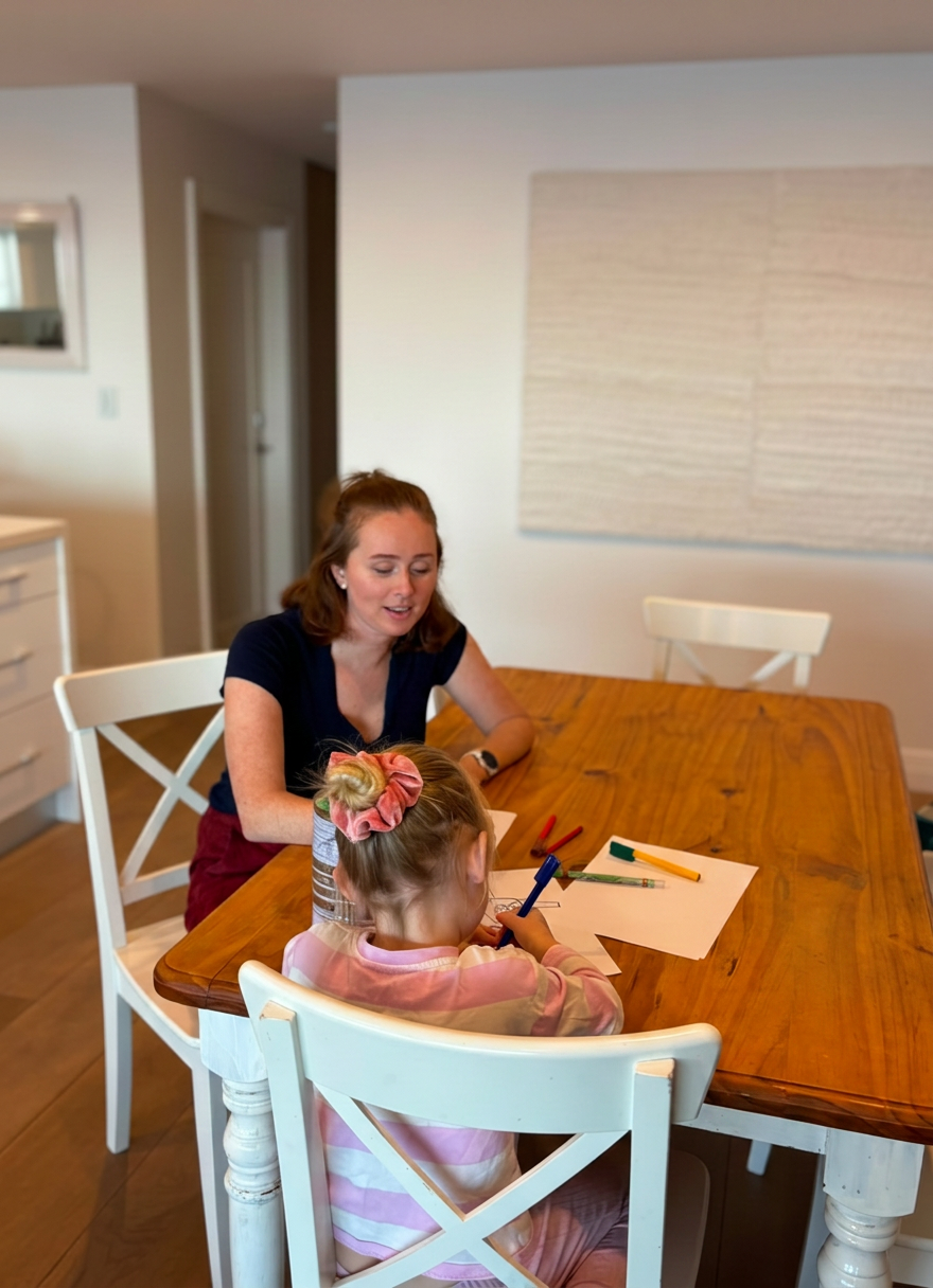 Woman and child drawing together at a wooden dining table.