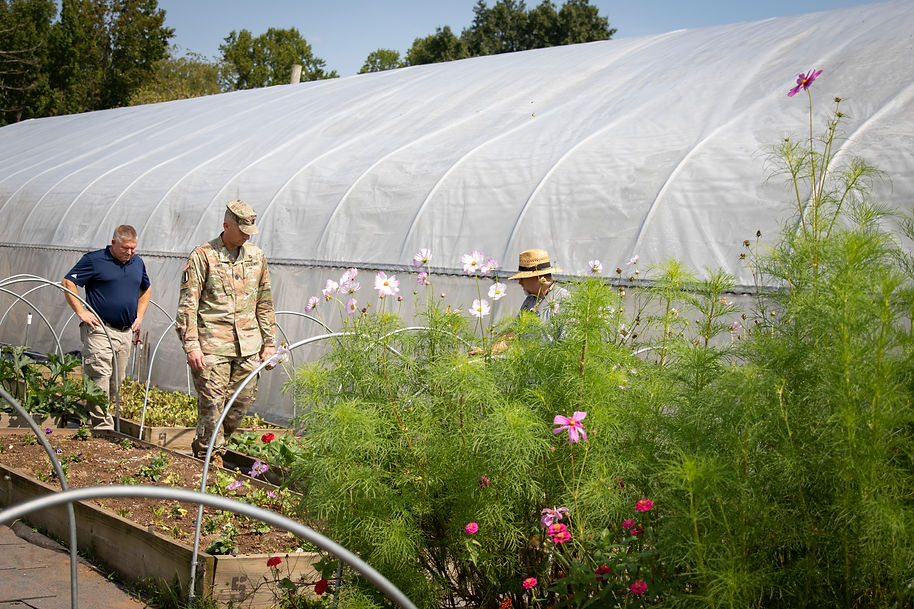 Two men looking at flowering raised beds in front of a high tunnel.