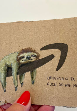 Gemaltes Faultier auf Amazon-Pfeil, Spruch: „Langweilst du dich auch so wie mich?“ auf braunem Karton