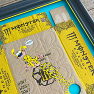 Handgemaltes Bild auf gelber Energy-Drink-Pappe: Das Comicwesen Marsupilami mit langem, gelbem Schwanz hüpft durch das Bild, Sprechblase „Houba!“. Text auf der Pappe: „Don’t worry, don’t cry, drink yello & fly“.