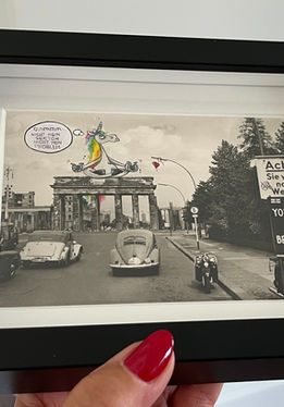 maleola-Postkarte mit Einhorn im Lotussitz und Zauberstab über dem Brandenburger Tor in Berlin – fantasievolle, humorvolle Collage