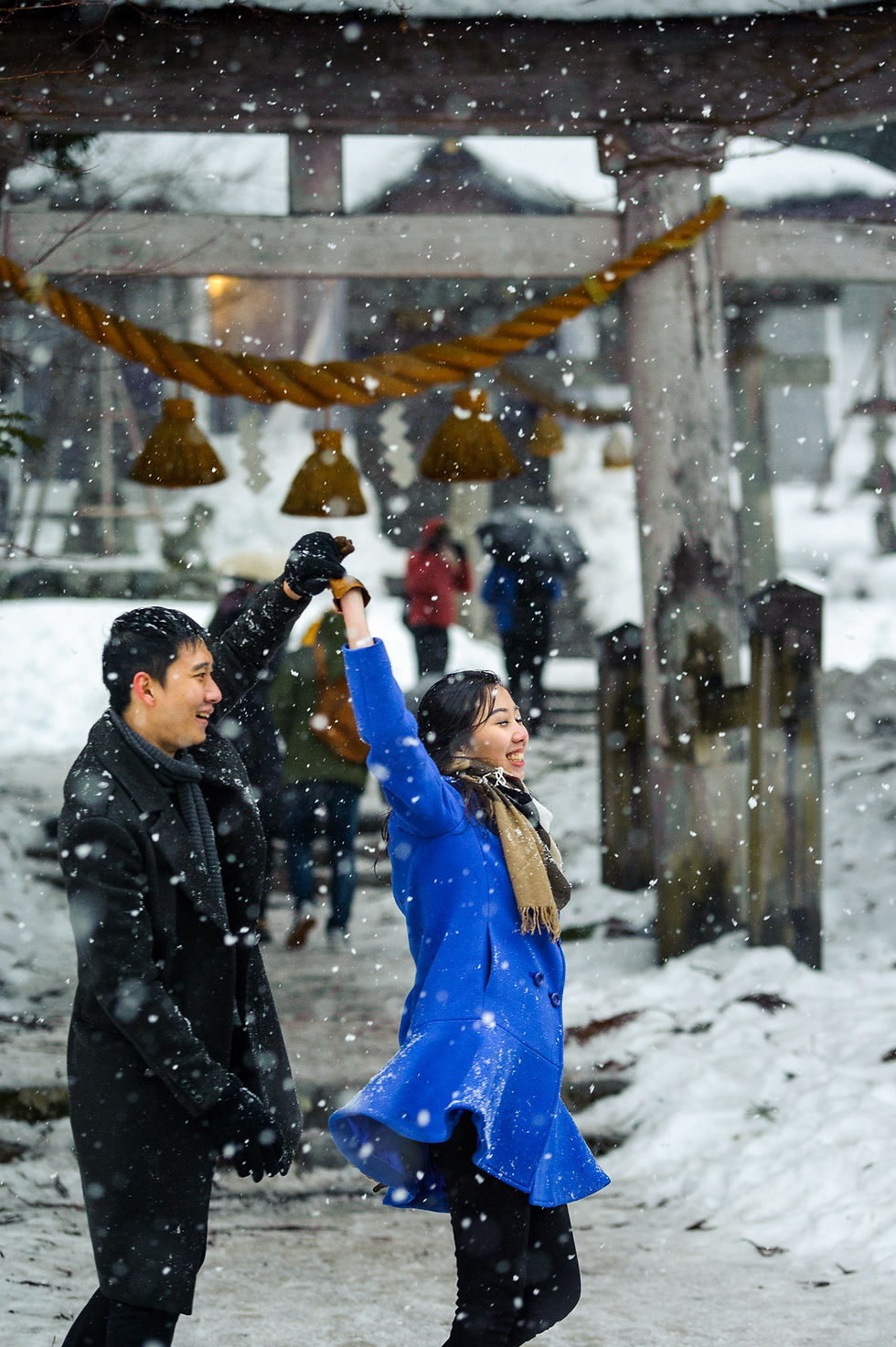 The snow falls around the couple as they dance in front of the torii gate