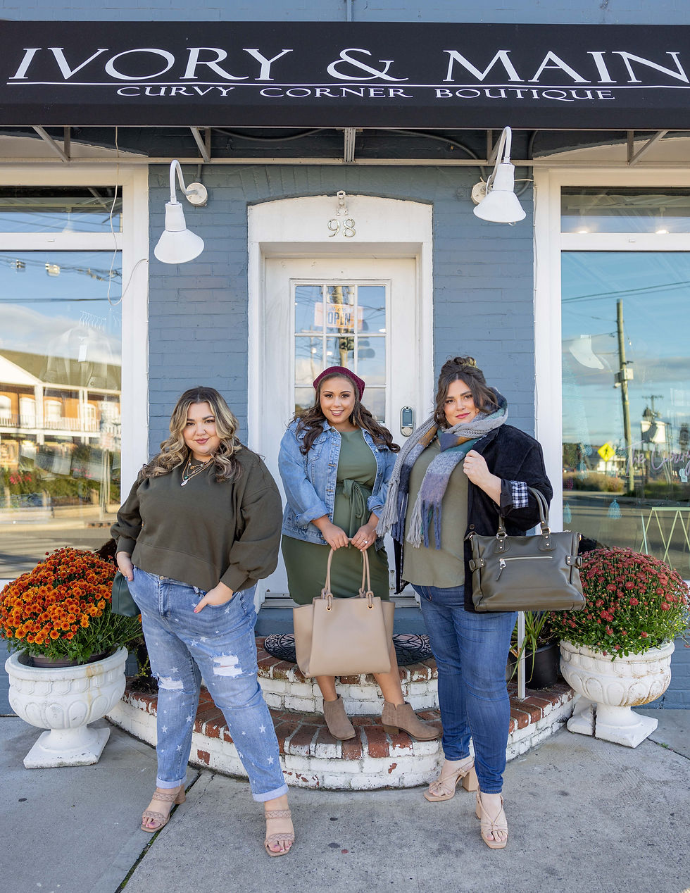 Three people pose in front of a boutique entrance with "Ivory & Main" above. They're wearing casual outfits, with flowers nearby.