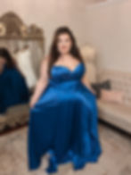 Woman in a vibrant blue gown smiles in a boutique, with elegant mirrors and dresses in the background. Cozy and elegant atmosphere.