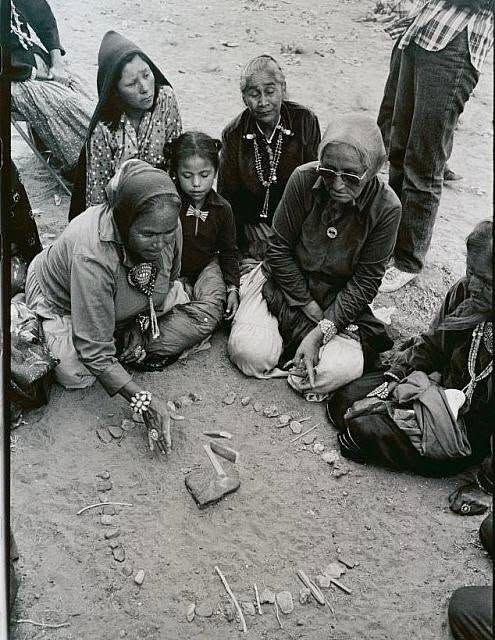 Diné women and a young girl gathered around stones while playing Tsidil in Chilchinbeto on the Navajo Nation in 1980.