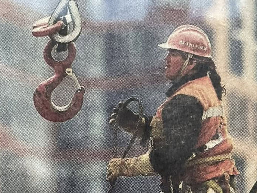 Two ironworkers in hard hats and safety gear stand on steel beams high above a World Trade Center construction site, representing Mohawk high-iron work and Indigenous contributions to modern infrastructure.