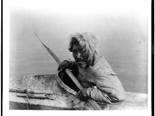 Black-and-white photograph of a Noatak seal hunter seated in a kayak while holding a paddle.
