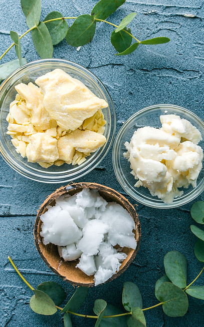 Shea butter and oils, displayed in bowls, with leaves on a blue surface.