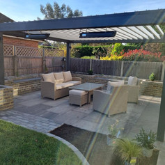 A lovey image of a full garden remodel with patio, plant boxes and a pergola with garden furniture to complete the new look