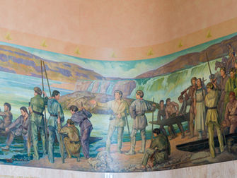 Two explorers stand on a river beach, surrounded by White men with canoes, a Native American woman, and, on the edge of the mural, Native American men on horses and a seated black man.