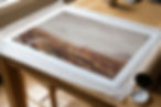 Landscape print laid out on a wooden table with wrapping paper and tube nearby, in a quiet workspace