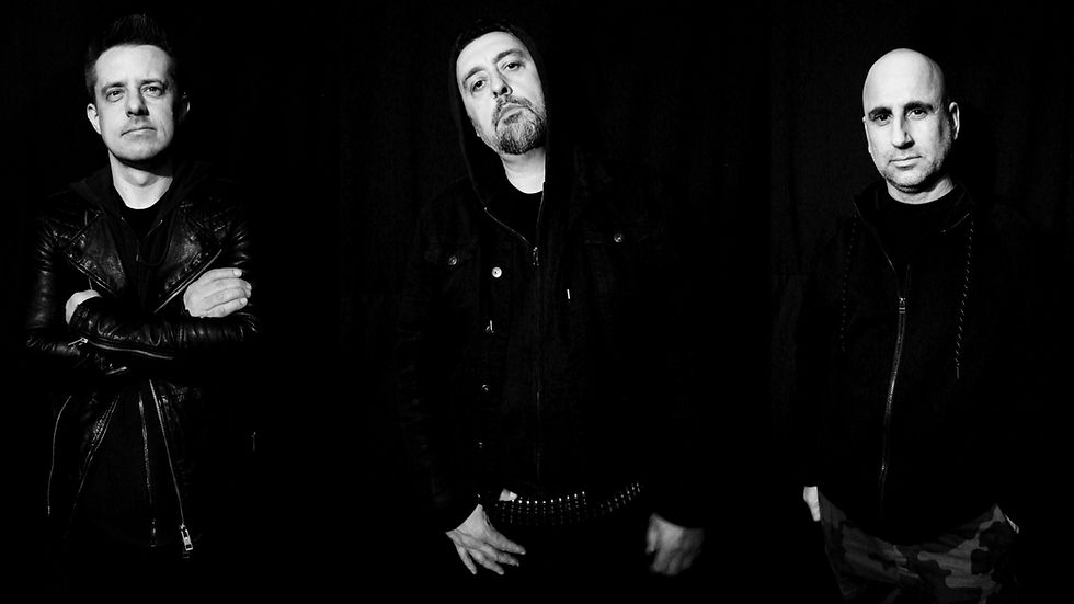 Three men in black jackets stand against a dark background, two with arms crossed, one with a hood, exuding a serious mood.