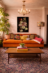 Colourful living room with burnt orange sofa, vintage rug, crystal chandelier, botanical wall art and layered textiles in a warm, characterful interior.