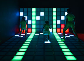 Players navigating on illuminated LED green pathways with colorful illuminated wall grid featuring strategically placed safe zones at LAVALED interactive experience in Chaweng, Koh Samui