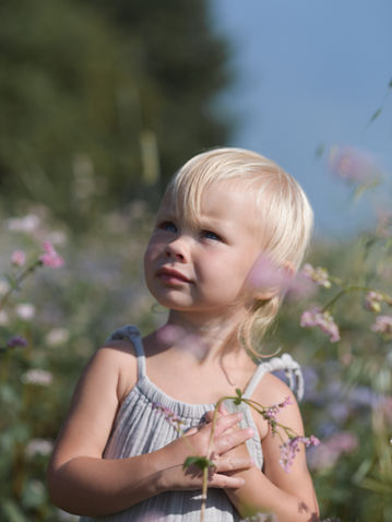 Ein Kind steht im hohen Gras mit violetten Blumen