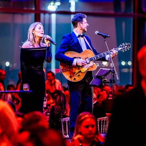 Live music duo in formal evening wear performing at a corporate award ceremony in a festive ballroom
