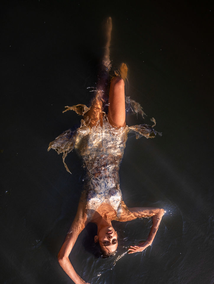 beautiful female model floating in green water, wearing a flowy dress