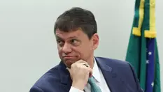 Esta imagem mostra Tarcísio de Freitas, atual Governador do estado de São Paulo, em um evento oficial com a bandeira do Brasil ao fundo.