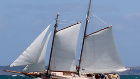 Classic wooden schooner sailboat under full sail in open water.