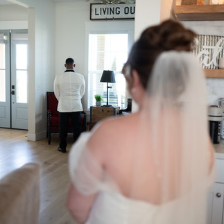Bride looks at groom who is facing away across the room 