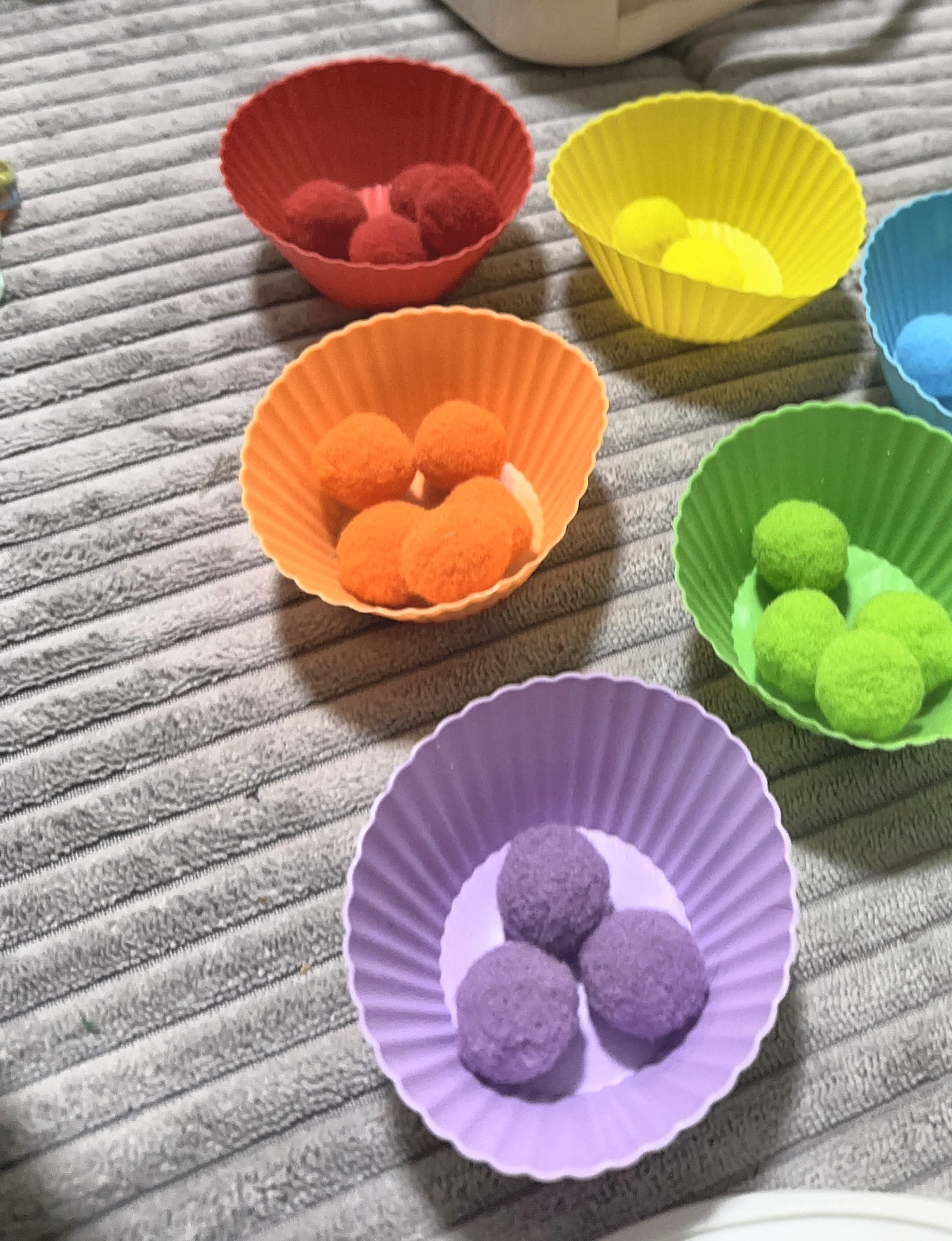 Sortierspiel mit Filzkugeln und Muffinförmchen in Regenbogenfarben