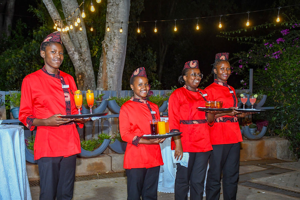 Four smiling servers in red uniforms hold trays of drinks under string lights in a garden setting.