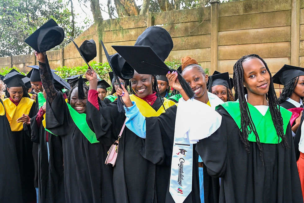 Smiling graduates in black gowns lift caps at an outdoor ceremony, with green and yellow stoles and a Congratulations sash.