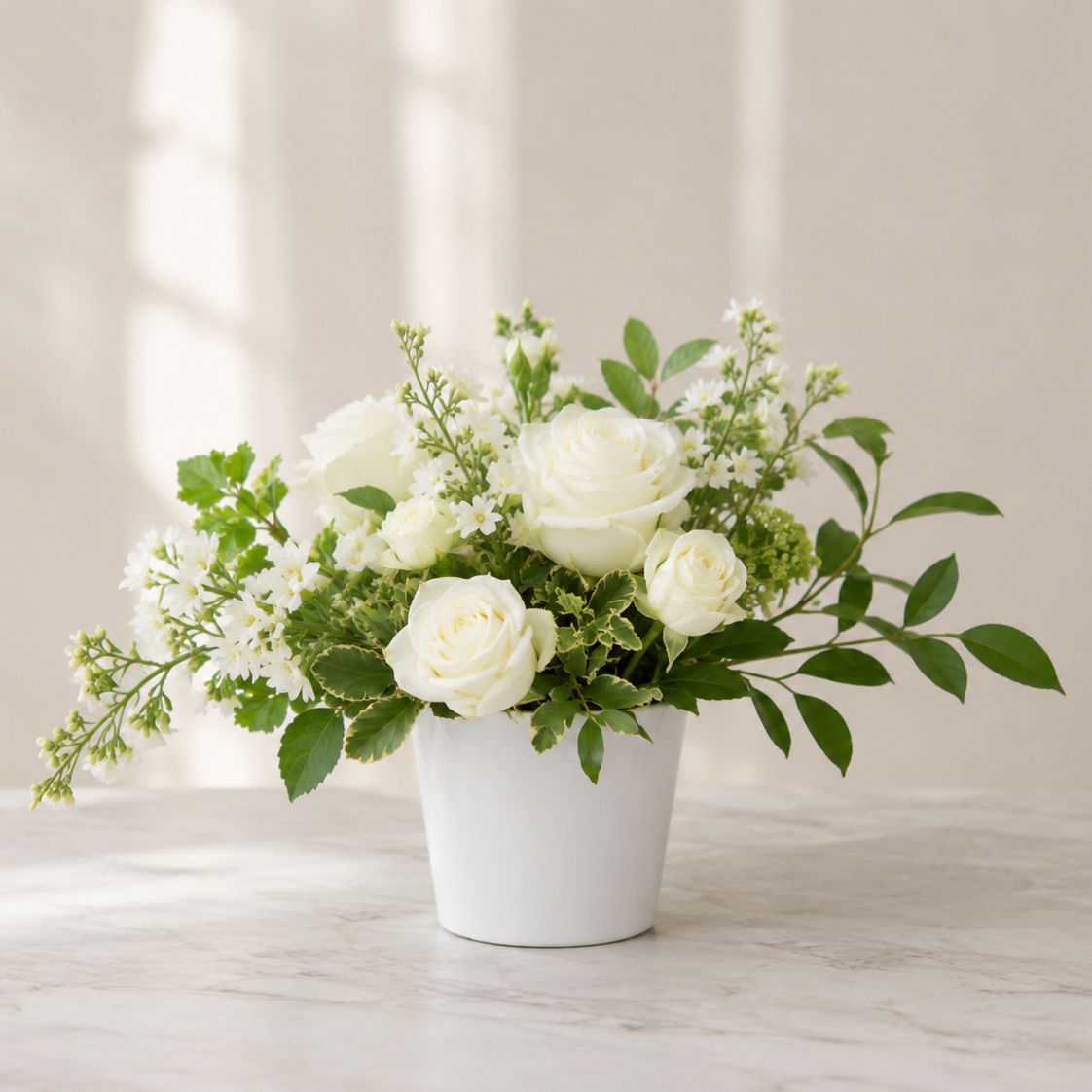 Classic Garden accent arrangement featuring white roses, seasonal blooms, and garden greenery arranged in a white vessel.