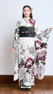 高知のきもの処公文、振袖展の新作「HIBIKI 6342」の全身写真。白地（クリーム色）に大きな紫の花柄が描かれた振袖を着用し、黒い帯を締めたモデルの立ち姿。長い髪に金の髪飾りをつけ、真っ直ぐにこちらを見つめる表情が、ハタチのヒロインの凛としたクールな美しさと大人っぽい魅力を表現しています。