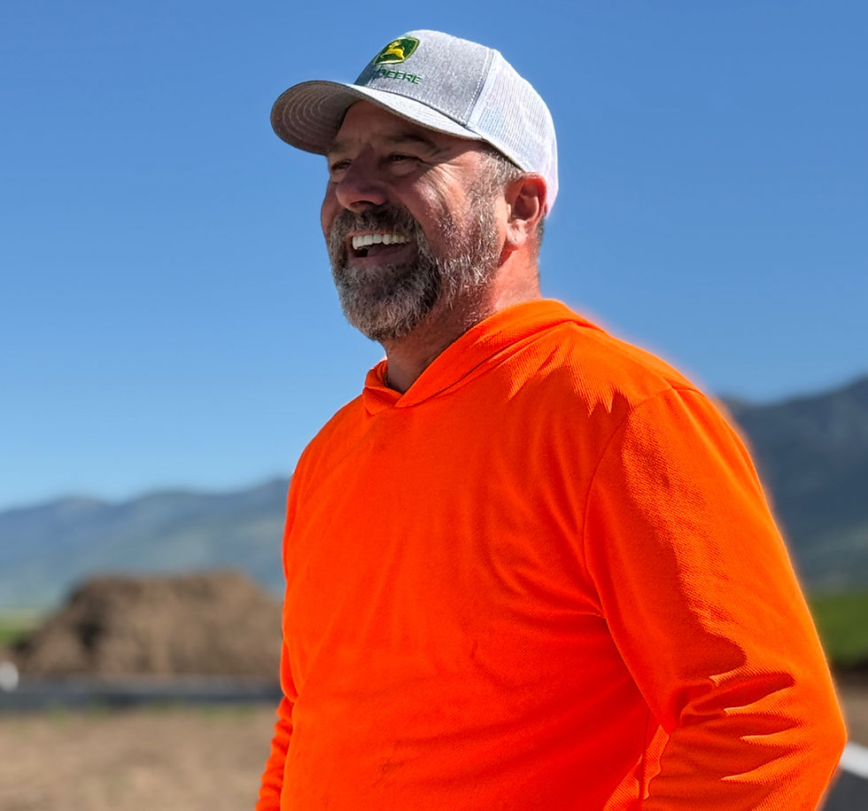 A construction worker in fluorescent orange laughing in front of a recently poured concrete foundation.