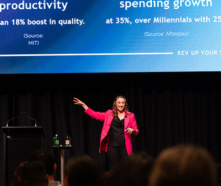 Abbie White (also searched as Abbey or Abby White) in a hot pink blazer, speaking onstage with one arm raised.