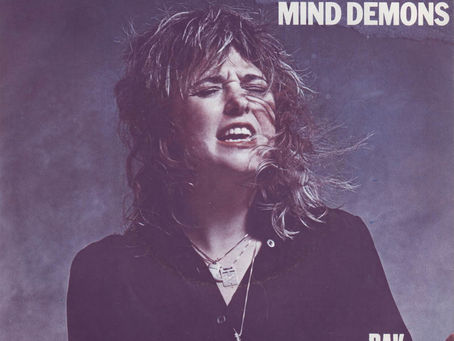 A dramatic portrait of Suzi Quatro singing intensely, with bold red and white text reading “Suzi Quatro – Mama’s Boy / Mind Demons.”