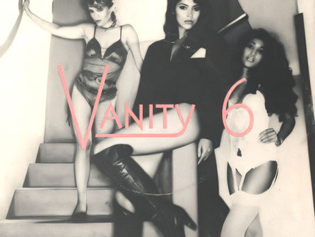 Black‑and‑white Vanity 6 cover featuring the trio posed on a staircase with bold pink “Vanity 6” lettering and the title “He’s So Dull.