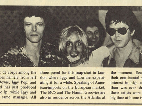 A black‑and‑white photograph of David Bowie, Iggy Pop, and Lou Reed standing together in London, arms around each other, during a period when all three were active in the underground rock scene.