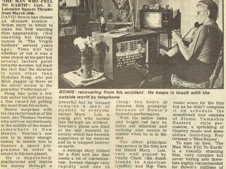 A black‑and‑white photograph of David Bowie seated indoors, speaking on a telephone while watching a television, used to illustrate a 1976 review of The Man Who Fell to Earth.