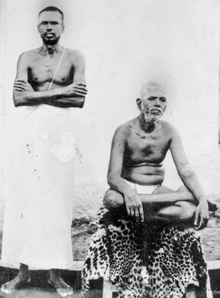 Two men, one standing with arms crossed, the other seated cross-legged on a leopard print fabric. Black and white, serene expressions.