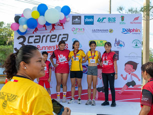 Premiación a corredoras en el podio de la 3ra Carrera Red Runners Kids, con fondo de patrocinadores y globos decorativos.