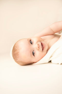 Close-up of a baby with a wide, toothless grin, captured mid-giggle in a relaxed studio shoot.