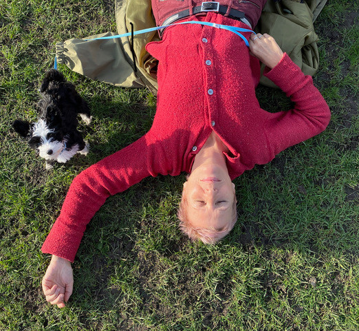 smiling woman lying on lawn with a puppy