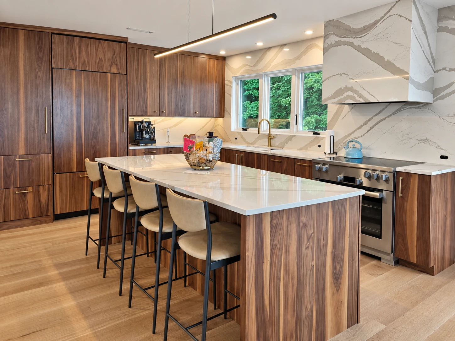Linear island pendant and recessed ceiling lights in the Quechee kitchen with warm wood cabinetry and veined stone.