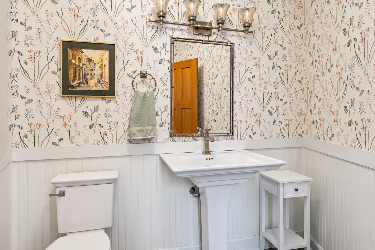 Botanical wallpaper above painted paneling with a pale blue pedestal basin.