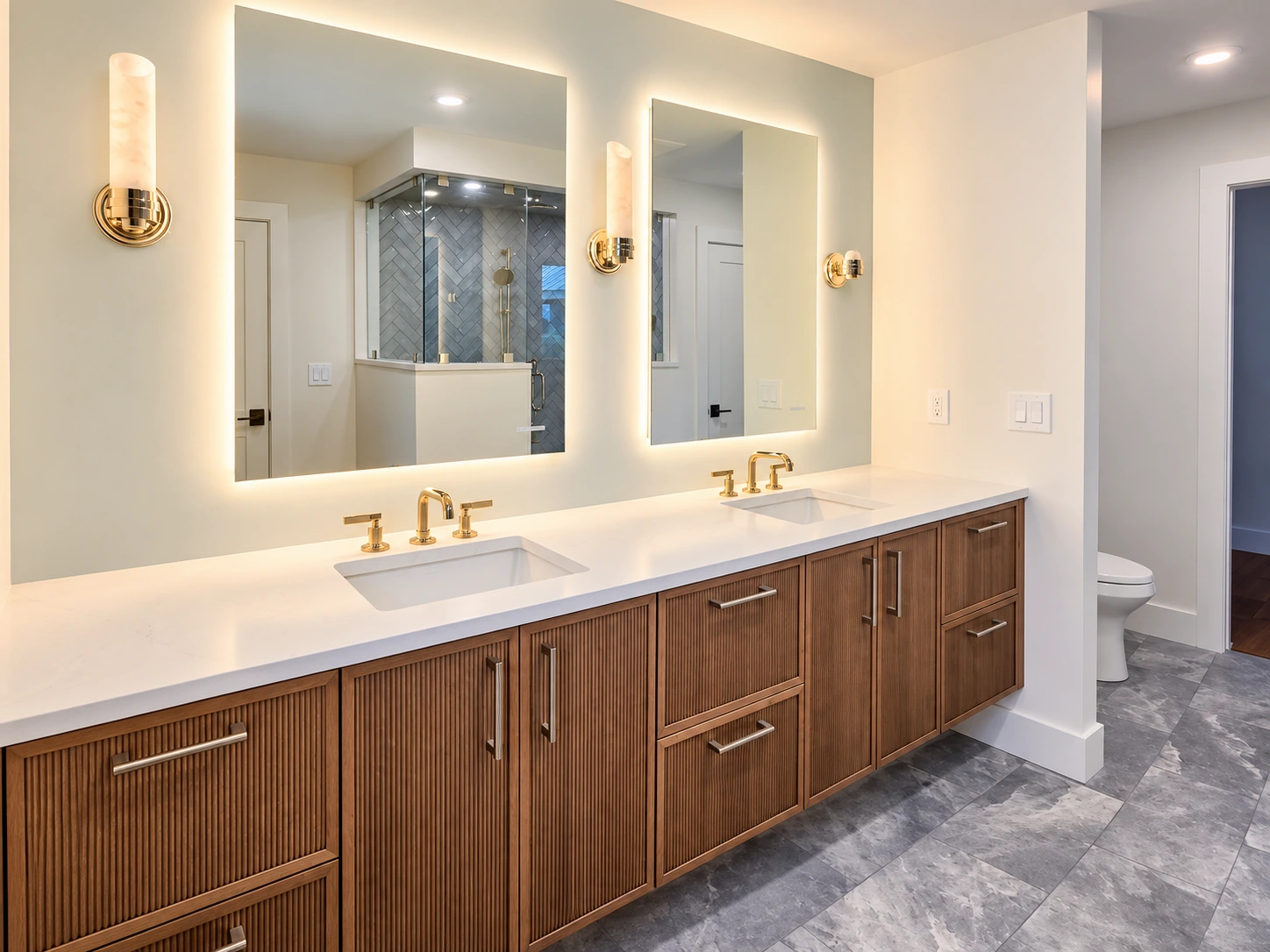Double wood vanity with illuminated mirrors and warm brass-toned lighting in Quechee.