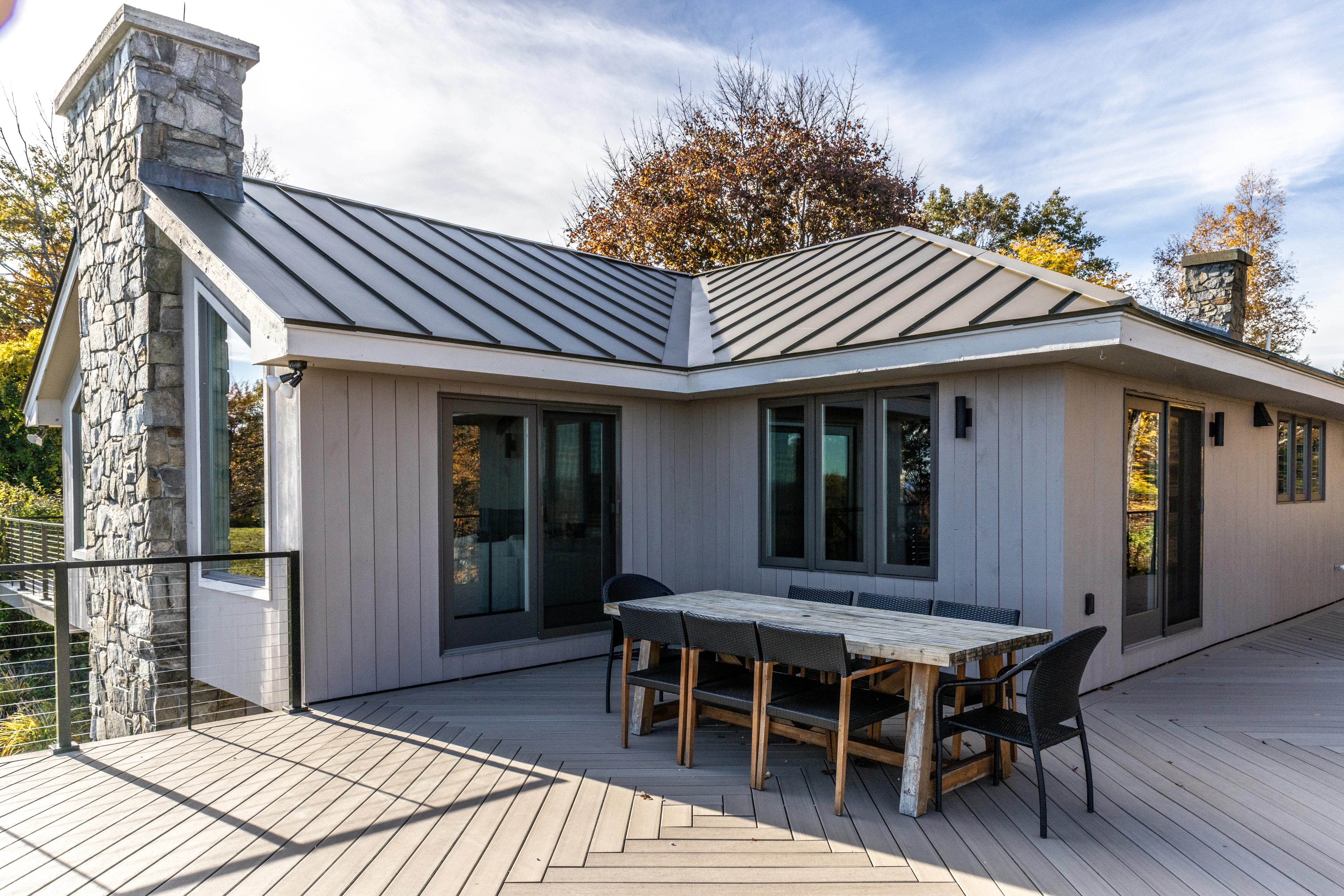 Stone chimney, standing-seam roof and outdoor dining on the deck at a Hudson renovation in Quechee, Vermont.