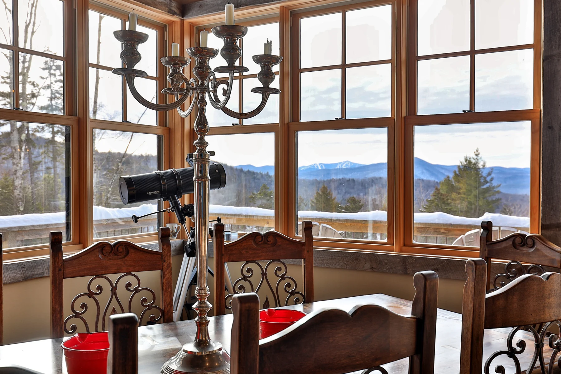 A wood dining table beside tall corner windows overlooking snow and distant mountains.