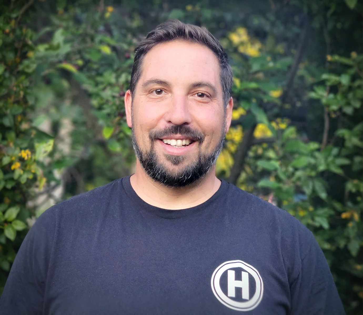 Patrick Hudson, founder of Hudson Design and Build, wearing the company's circle H logo shirt outdoors in Vermont.