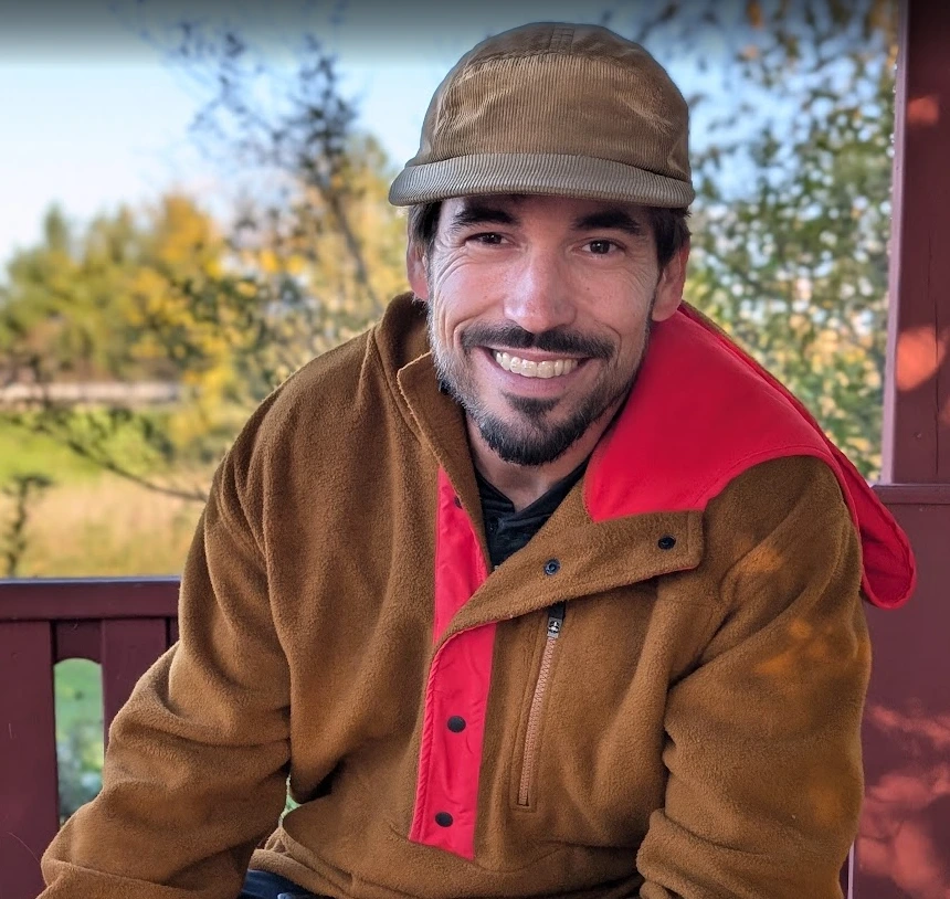 Jeremy Hudson, Managing Partner of Hudson Design and Build, outdoors in a brown cap and jacket with autumn trees behind him.