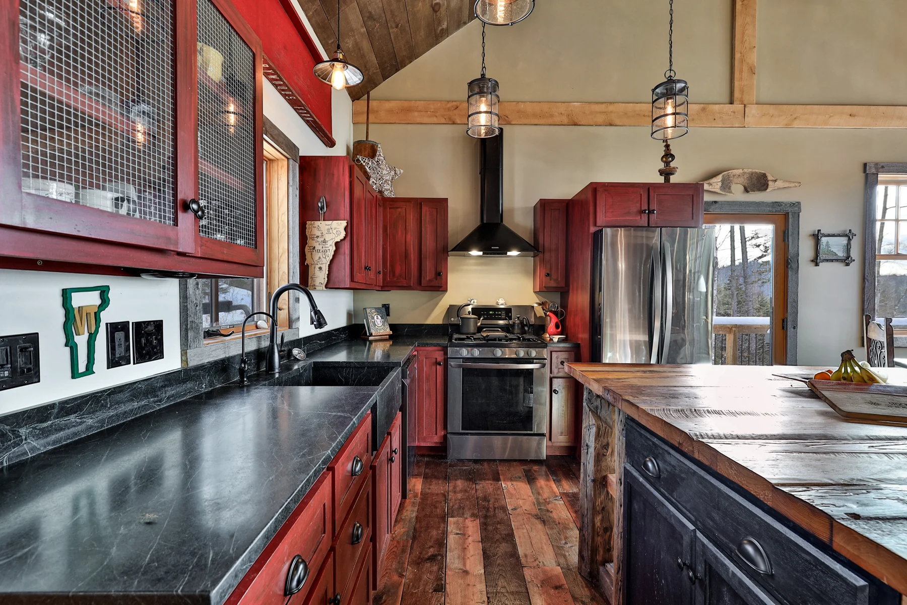 Rustic kitchen with red cabinetry, dark counters and a wood island in a Hudson Design and Build ski home near Killington, Vermont.